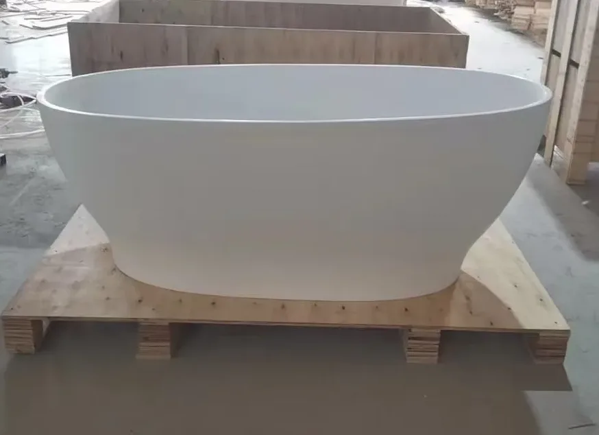 High-angle factory view of a freestanding solid surface bathtub highlighting the integrated slotted overflow and export-grade crating in the background.
