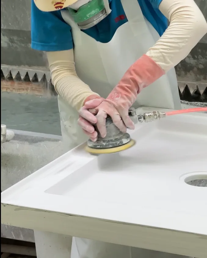 HONDAO factory technician using a pneumatic sander to calibrate the perfect drainage pitch on commercial Solid Surface Shower Pans.