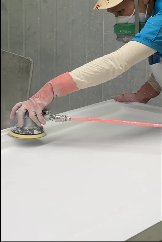 A factory technician hand-sanding a homogeneous solid surface Artificial Stone Shower Base to demonstrate on-site repairability.