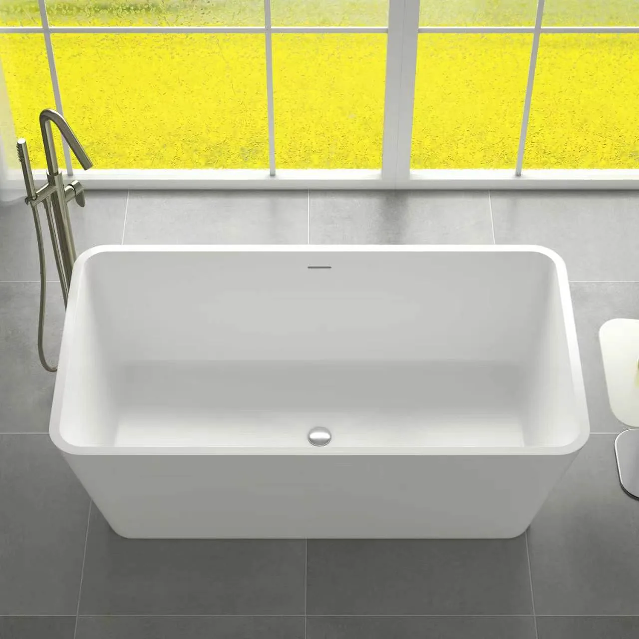 High-angle perspective view of the matte white tapered rectangular solid surface freestanding bathtub showcasing its modern geometric profile next to a large floor-to-ceiling window.